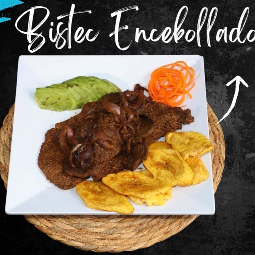 Bistec Encebollado with fried plantains, avocado slices, and shredded carrots on a white plate.
