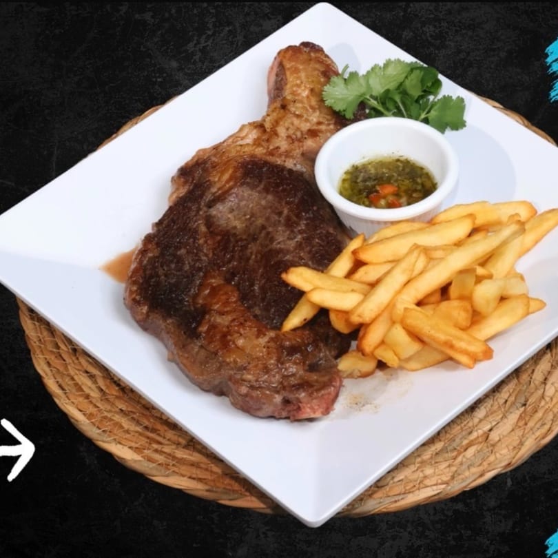 Grilled steak with a side of golden french fries, green sauce, and cilantro on a white plate.