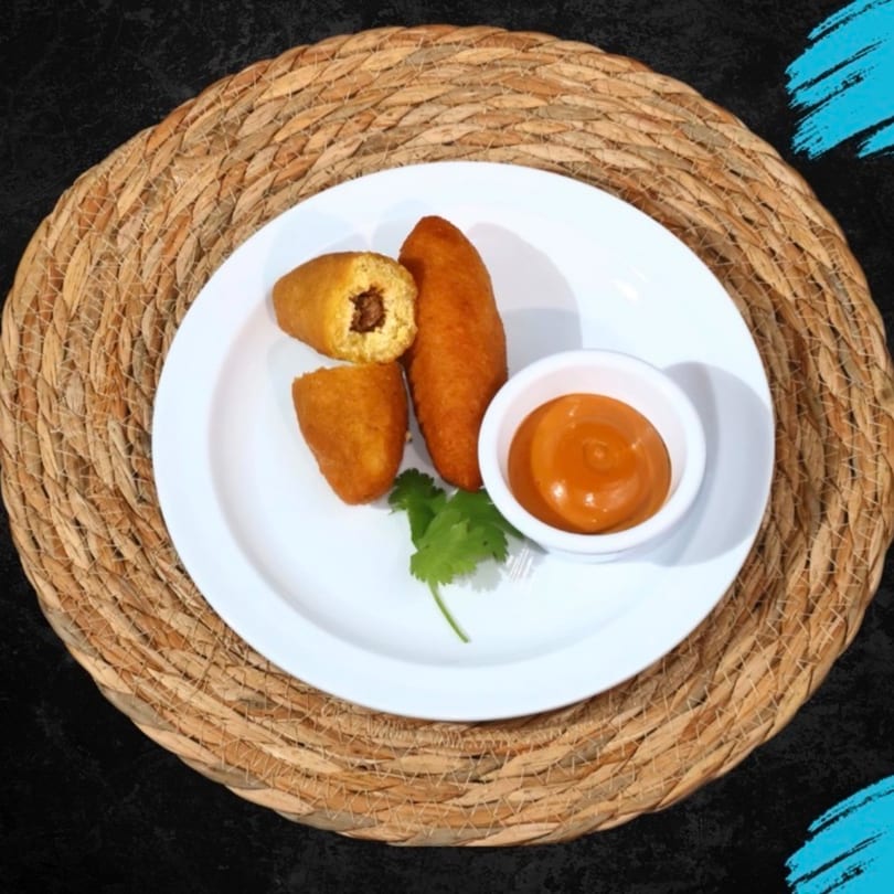 Three fried plantain empanadas, one cut open, with a side of orange sauce and cilantro.