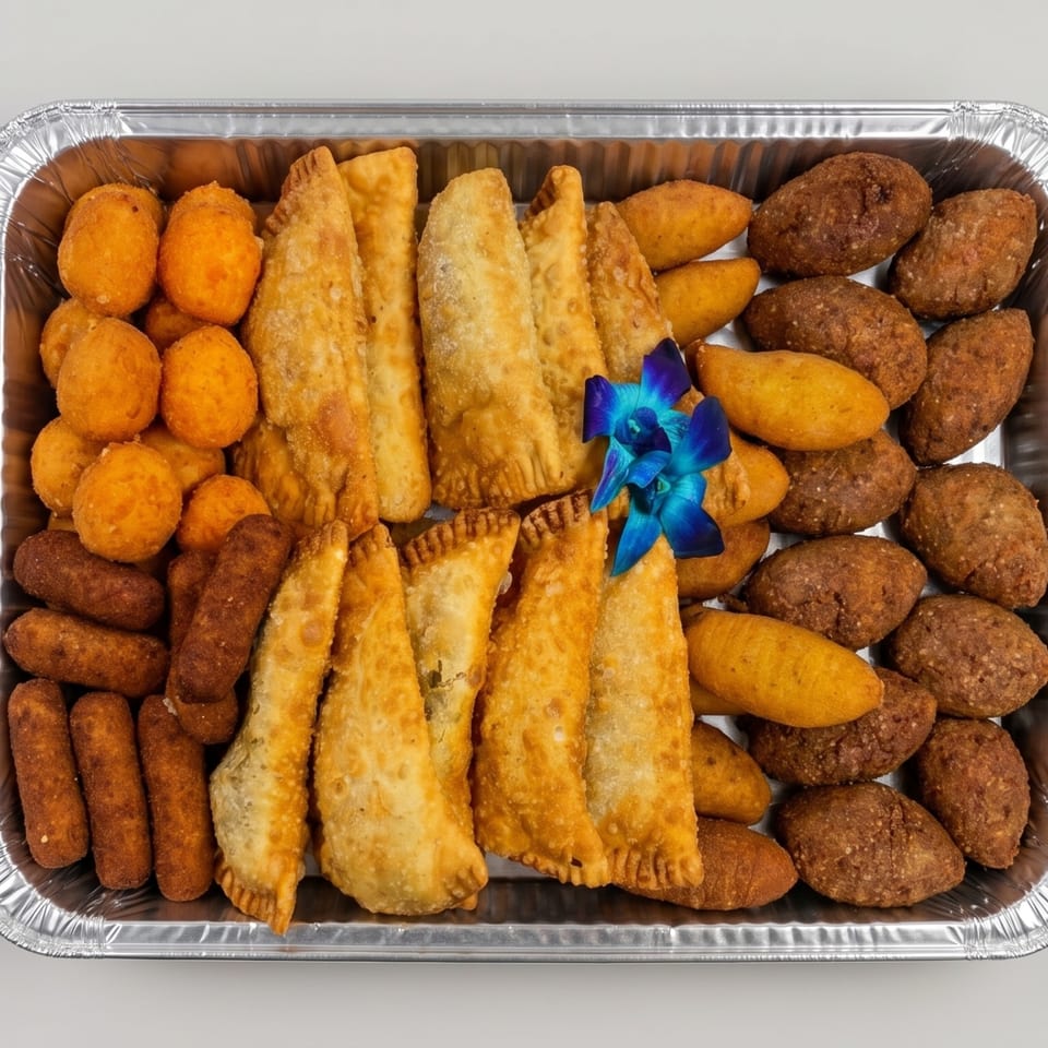 A catering tray filled with various fried appetizers, including empanadas, croquettes, and other savory pastries.
