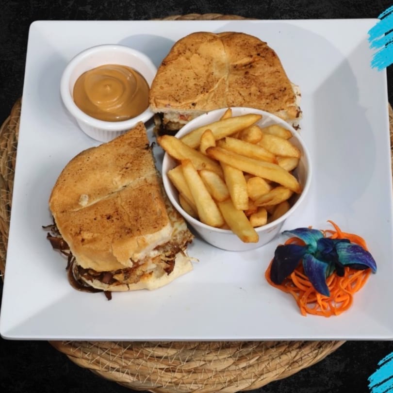 A sandwich cut in half, fries, dipping sauce, and blue orchid garnish on a white plate.